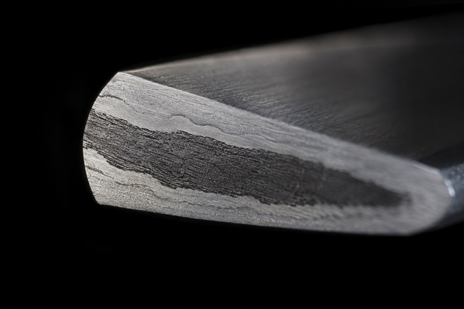 Macro photo of a blade's polished cross-section showing layered bands of light and dark steel